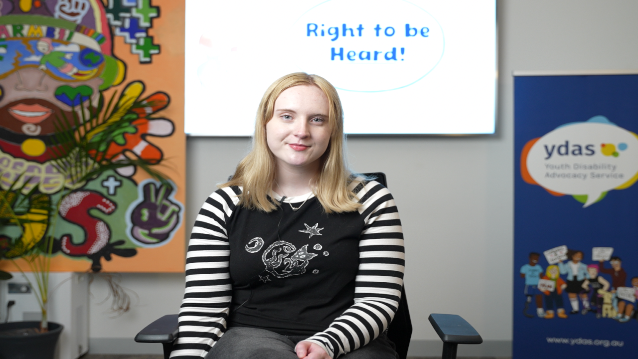 Photo of a white young person smiling at the camera, as if being interviewed