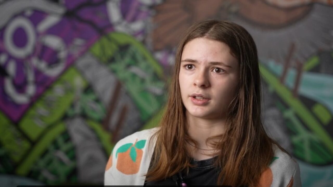 Photo of Thali, a white disabled young person, talking to the camera