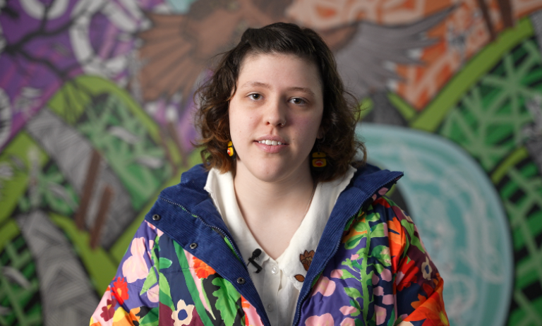 Willow, a disabled young person wearing a colourful jacket, looking at the camera.